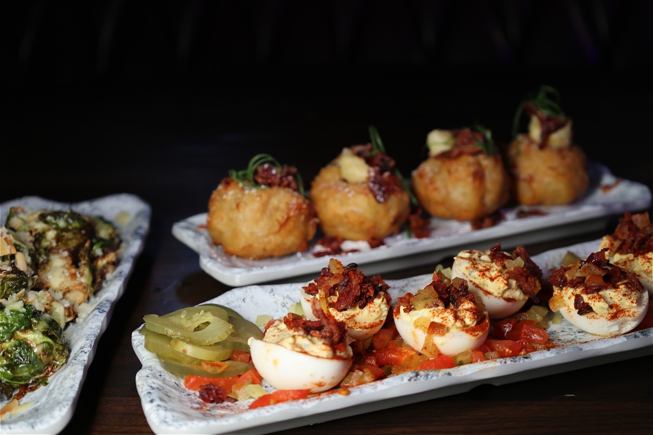 A plate of deviled eggs plated dark and close on marble, with a lit candle beside it.